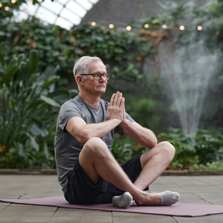 man sitting on yoga matt with palms clasped together