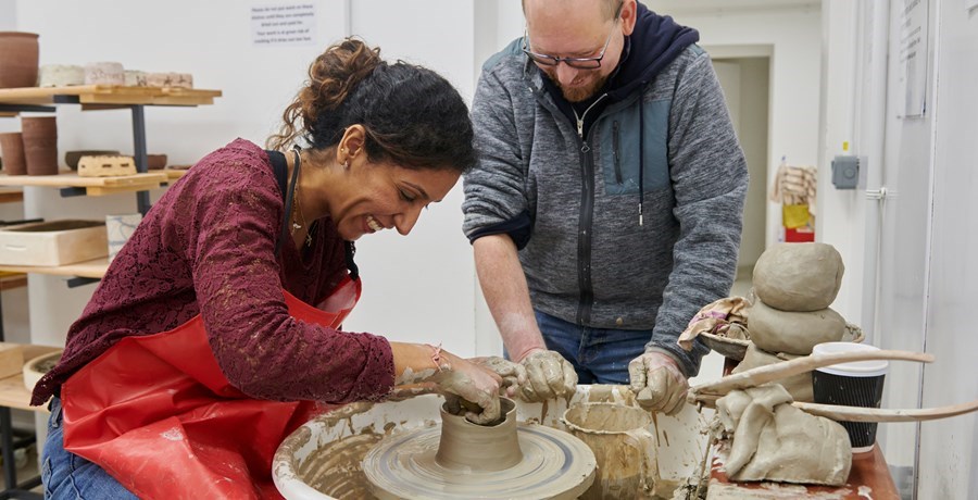 Lady in red apron at a pottery wheel working with clay