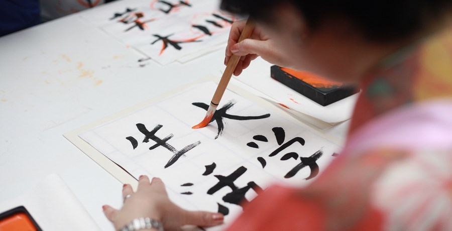 Woman using a brush to write Japanese characters on white paper