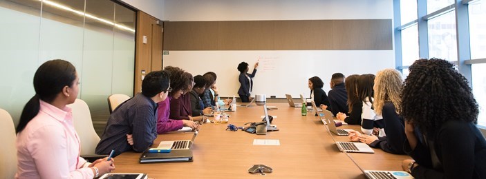 people sitting around a large desk looking towards a person standing